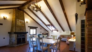 A dining area with a stone fireplace, wooden beams, and a chandelier.