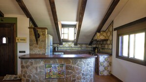 A kitchen with a stone island, wooden beams, and a view of the outdoors.