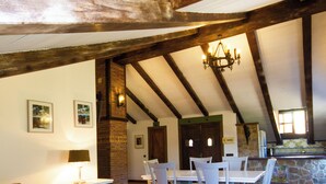 A dining area with a wooden ceiling, white furniture, and a stone wall.