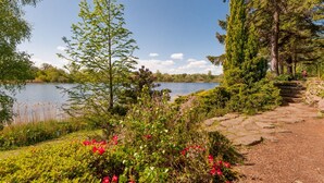 A lakeside garden with a stone pathway, lush greenery, and red flowers. - Beautiful Georgian property enjoying a quiet location. Sleeps 10. (Edinburgh)