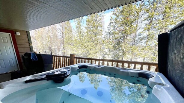 A hot tub on a wooden deck with a view of trees. - Alpine Bliss Awaits: Beautiful Mountain Home with Hot Tub (Kimberley)