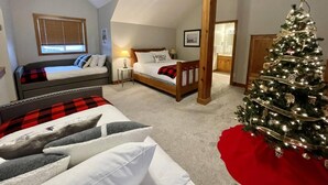 A cozy bedroom with two beds, a wooden ceiling, a Christmas tree, and a bathroom visible in the background. - Alpine Bliss Awaits: Beautiful Mountain Home with Hot Tub (Kimberley)