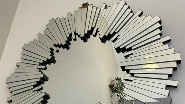 Ein runder Wandspiegel mit modernem Design, der ein zentrales schwarzes Muster und Metallelemente aufweist.