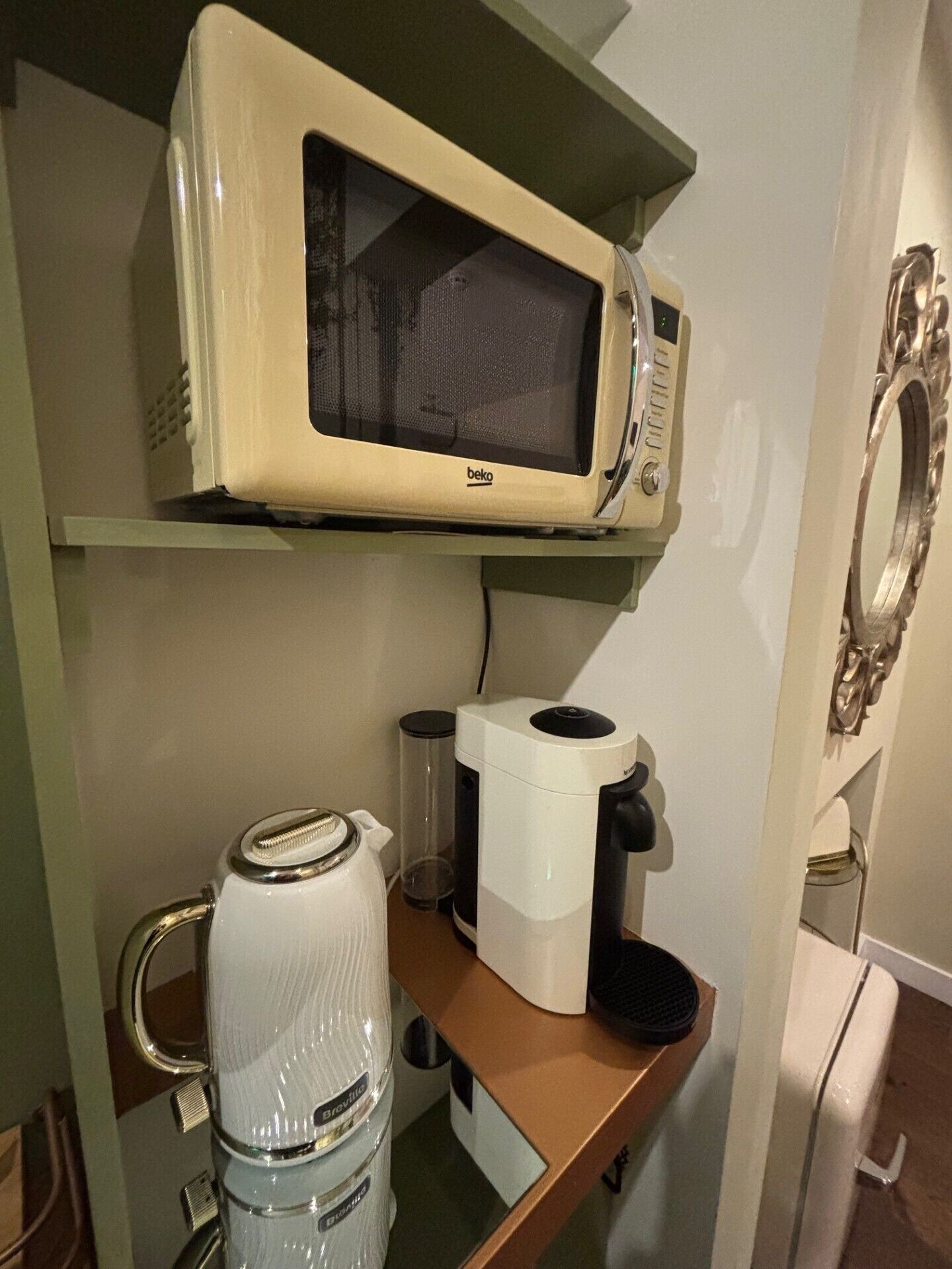 A kitchenette with a beige microwave, a coffee maker, and a water dispenser on a wooden countertop.