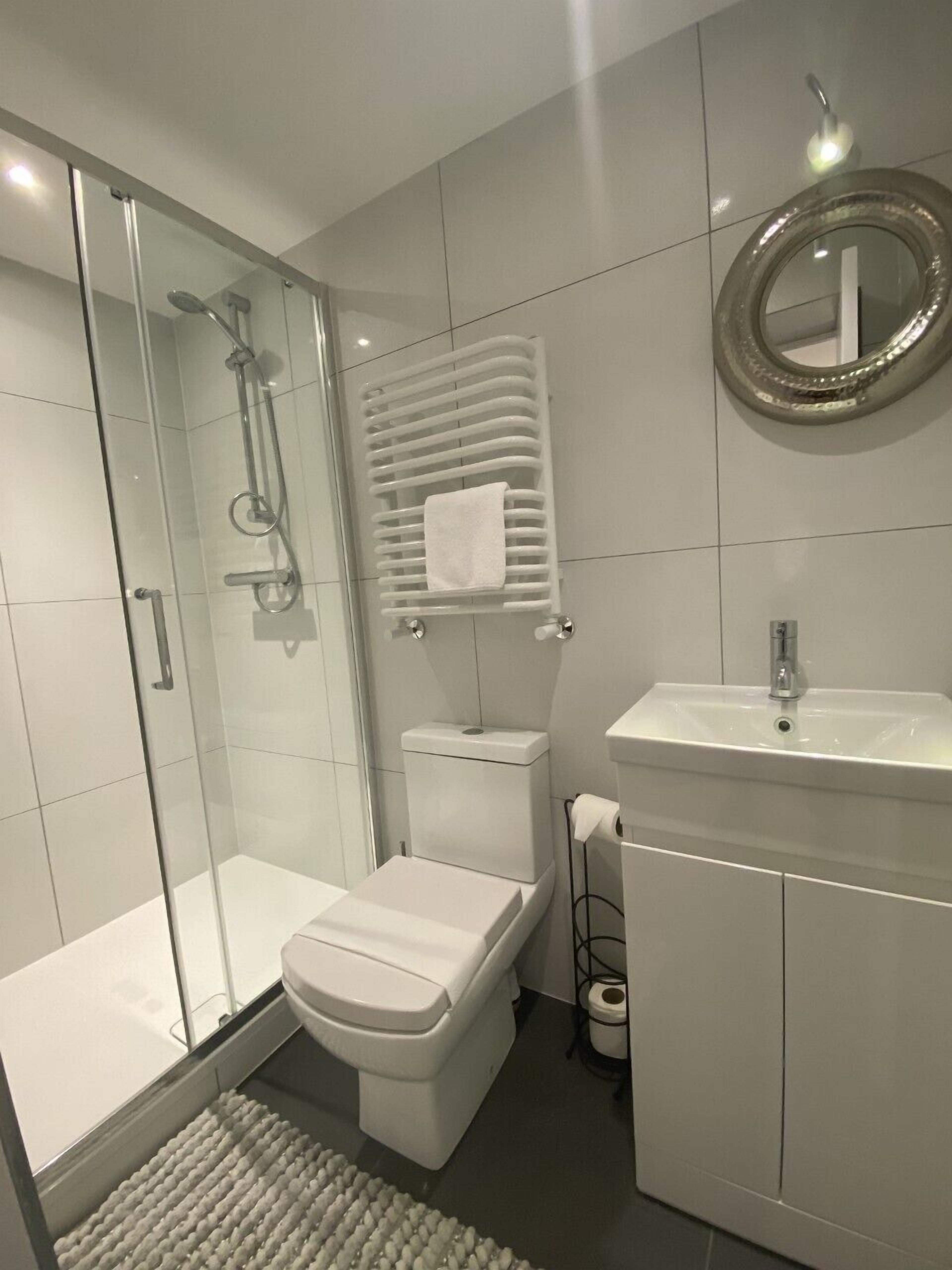 Een moderne badkamer met een douchecabine van glas, toilet, wastafel en spiegel.