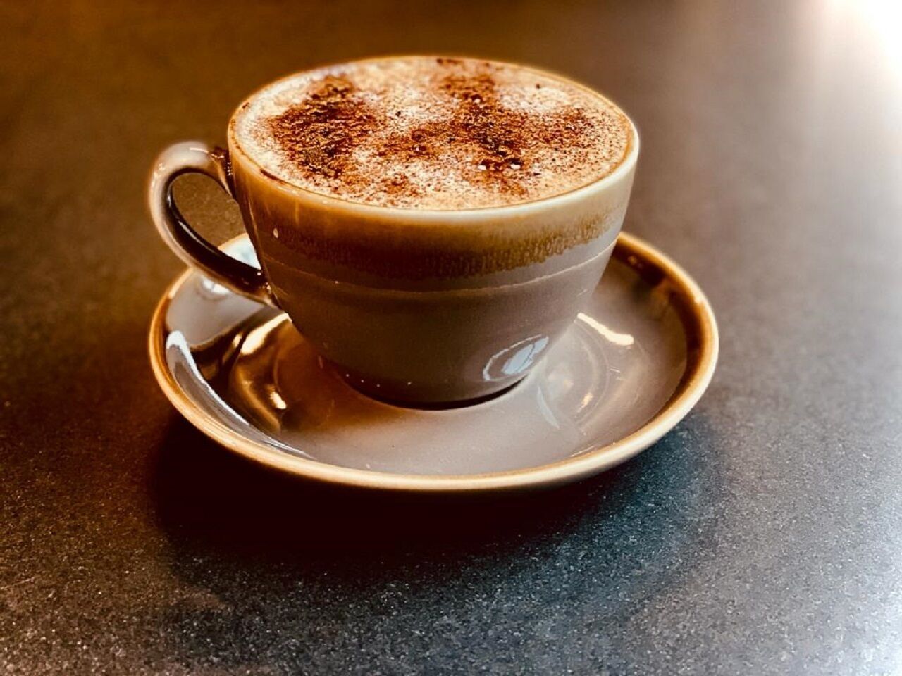 A cup of coffee with a frothy top, placed on a saucer.