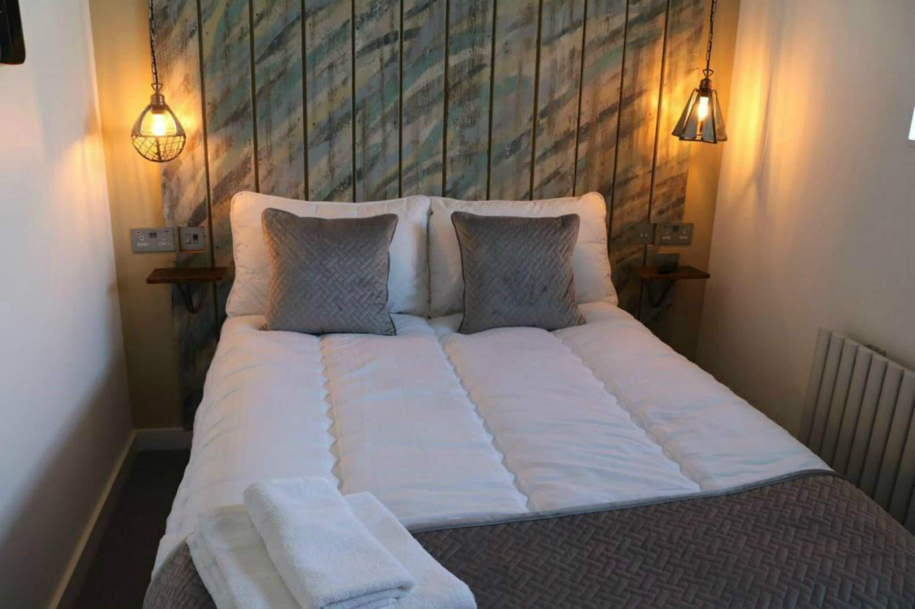 A neatly made bed with a white duvet and two pillows, flanked by two wall-mounted lamps.