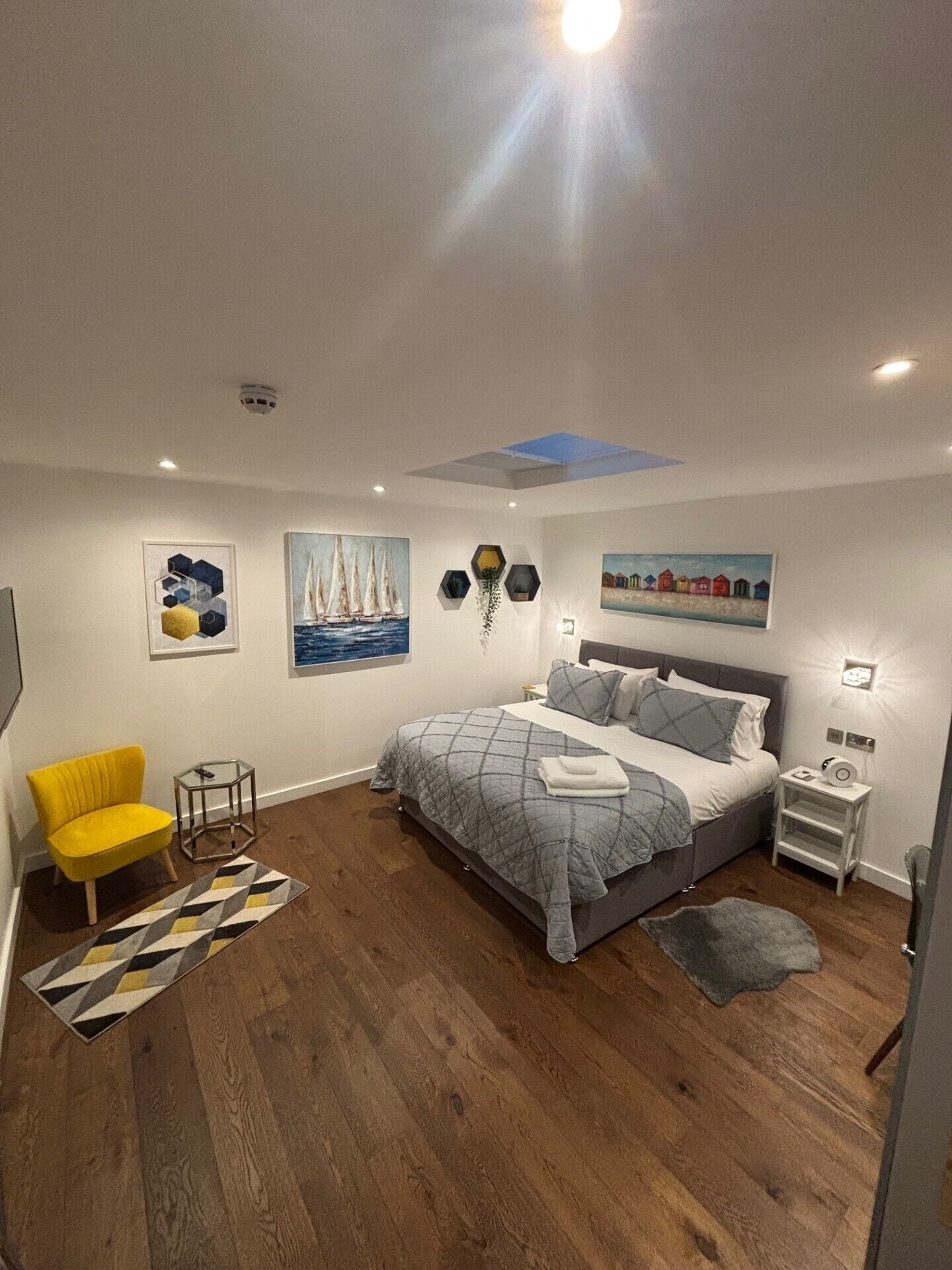 A modern bedroom with a bed, a yellow chair, and artwork on the walls.