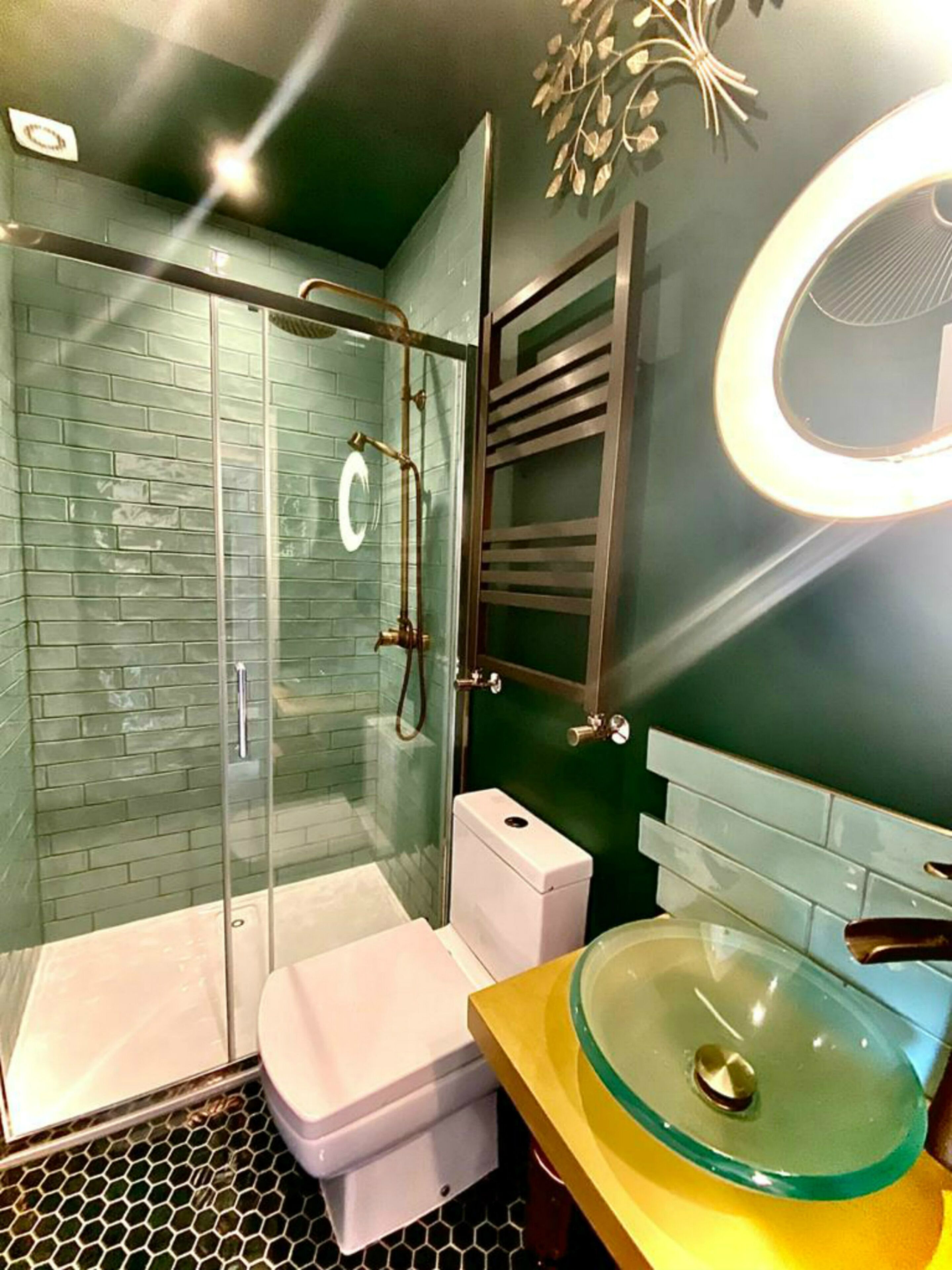 A modern bathroom with a glass shower enclosure, a white toilet, and a round glass sink with a yellow countertop.