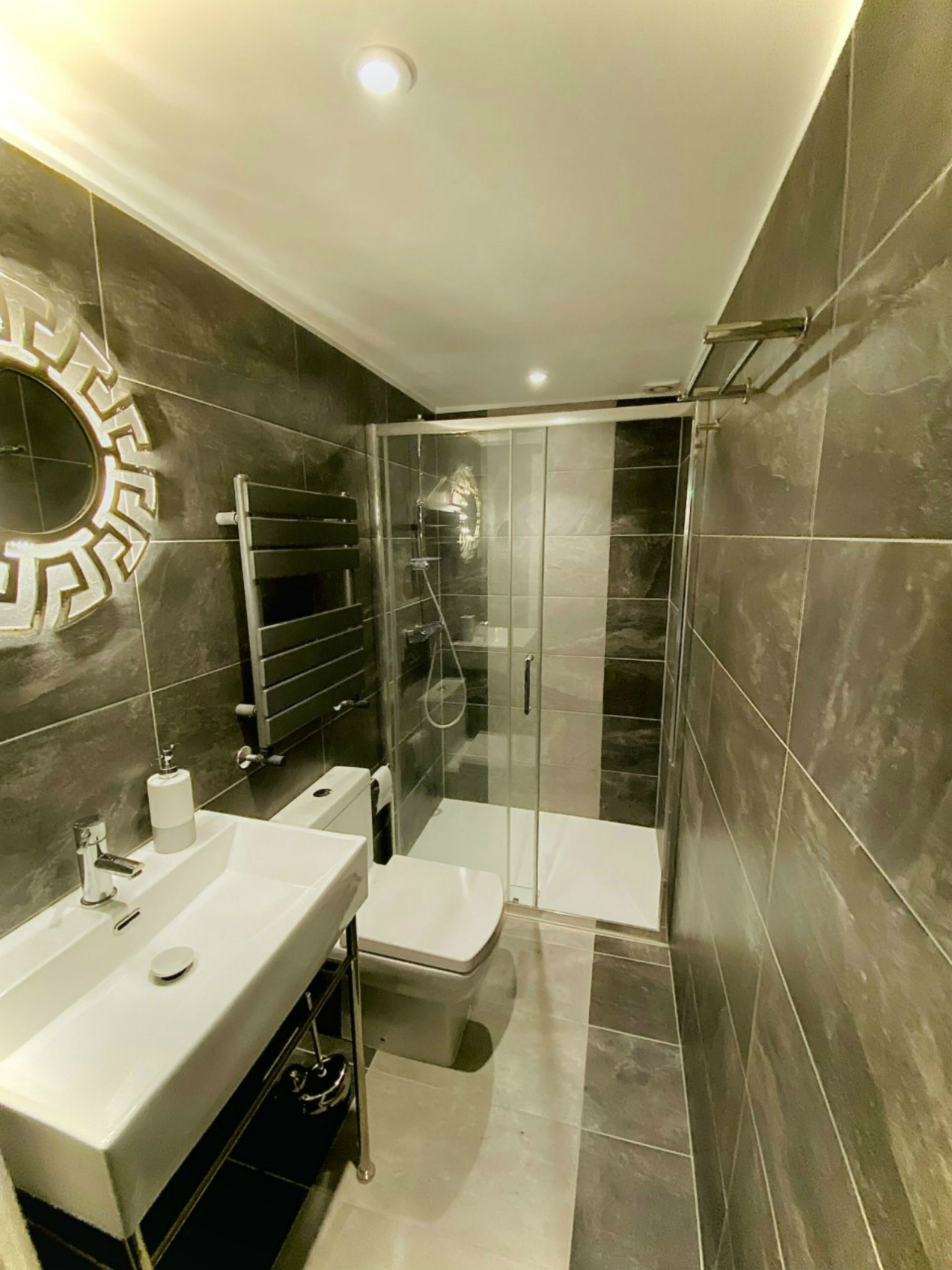 A modern bathroom with a glass-enclosed shower, a white sink, and a mirror with a decorative frame.