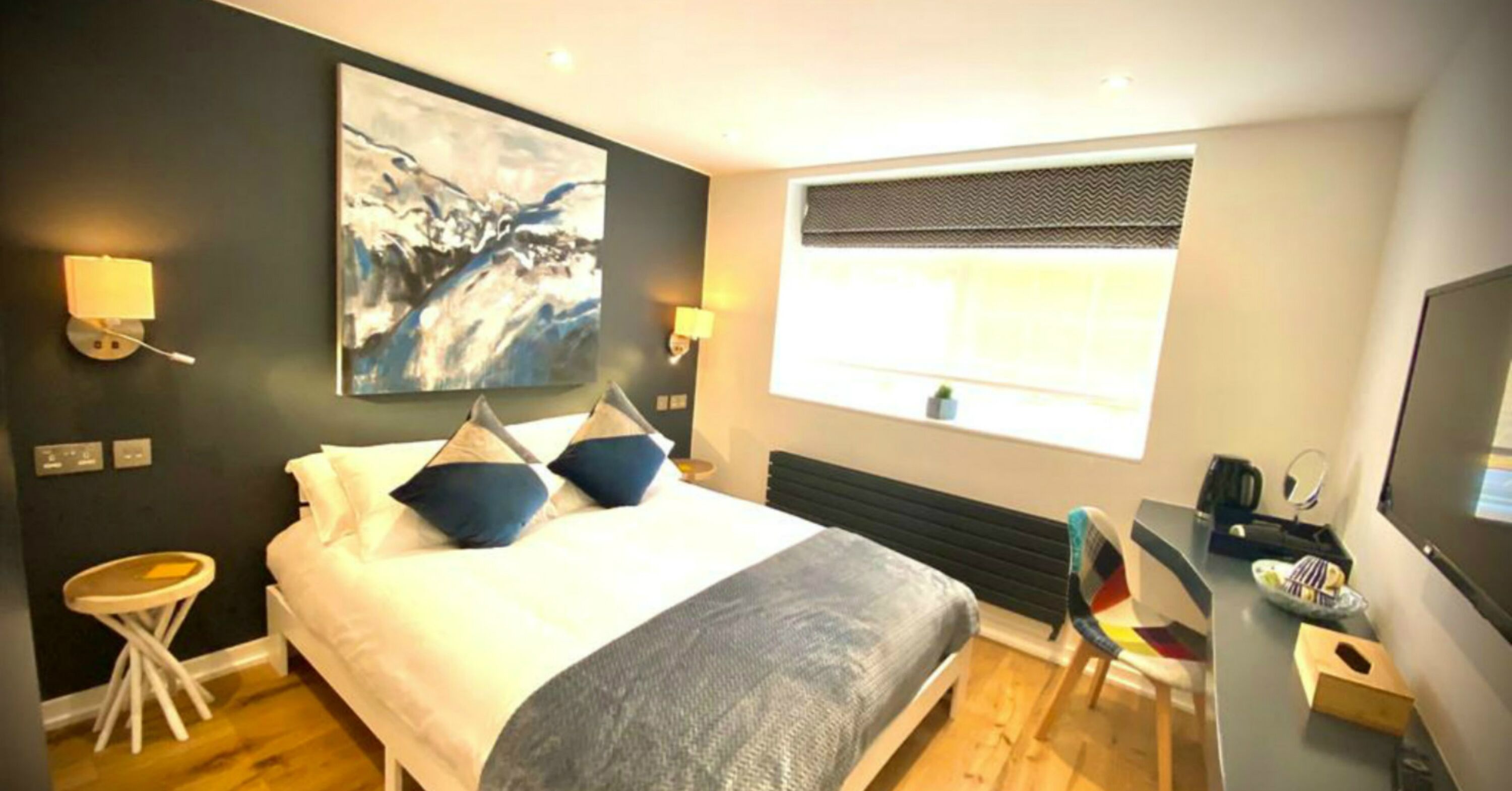 A modern hotel room with a large bed, a desk, a chair, and a television.