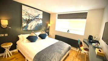 A modern hotel room with a large bed, a desk, a chair, and a television.
