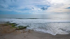 A beach with waves, rocks, and a cloudy sky. - Ocean Dunes 2123 (Kure Beach)