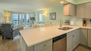 A modern kitchen with a central island, built-in appliances, and a dining area with a view. - Ocean Dunes 2123 (Kure Beach)