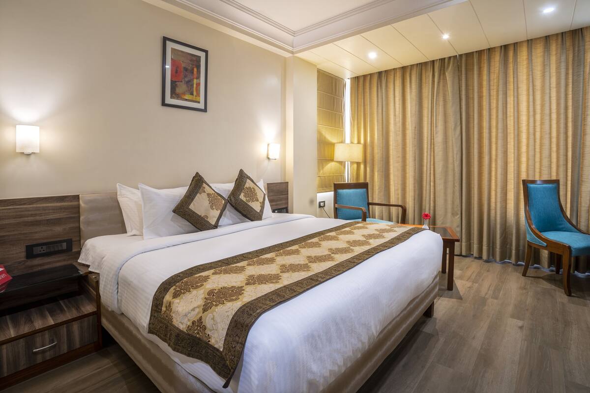 Een hotelkamer met een groot bed, een nachtkastje, een bureau, een stoel en een raam met gordijnen.