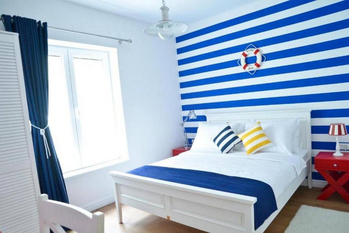 A bedroom with a bed, a nightstand, a lamp, a chair, and a window with curtains.