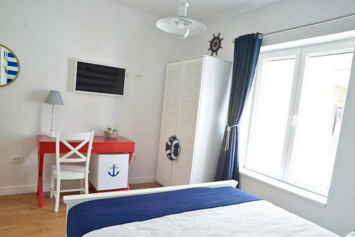 A bedroom with a bed, a desk, a chair, a wardrobe, and a window with curtains.
