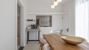 A modern kitchen with a wooden dining table, a coffee station, and a view into the living area. - Condo in the heart of town. (Bar Harbor)
