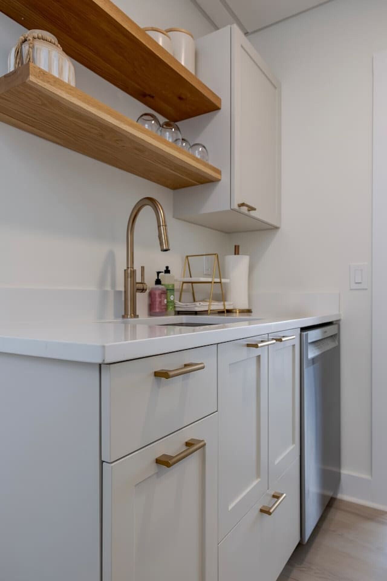 Een moderne keuken met witte kasten, een RVS vaatwasser en een houten plank boven de gootsteen.