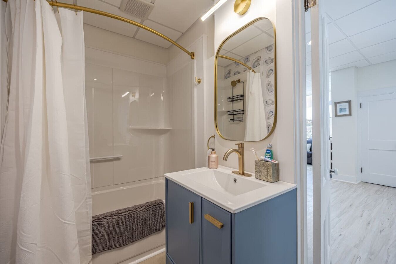 Een badkamer met een douche, een wastafel met gouden kraan, een spiegel met gouden lijst en een handdoekhouder.
