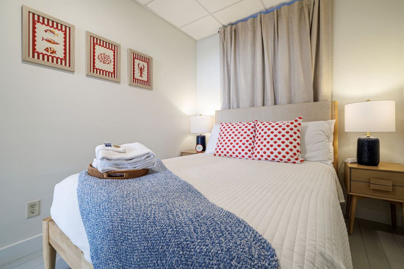 A hotel room with a bed, a nightstand, a lamp, a clock, and three framed pictures on the wall.