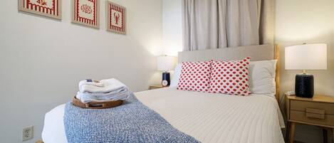 A hotel room with a bed, a nightstand, a lamp, a clock, and three framed pictures on the wall.