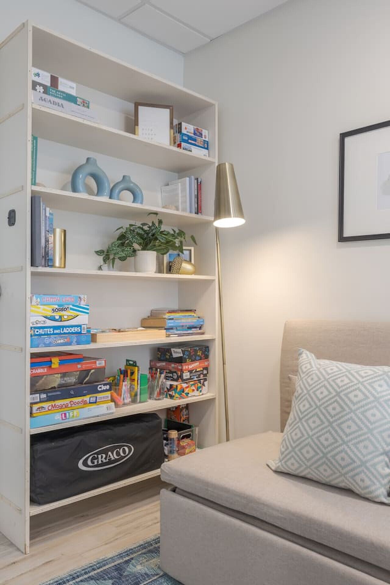 Ein Zimmer mit Bücherregal, Lampe, Sofa und einem gemusterten Kissen.