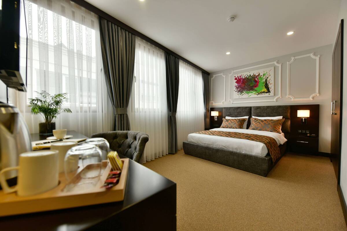 Hotelkamer met een bed, een bureau met een dienblad met ontbijtartikelen, een stoel, een potplant en een schilderij aan de muur.