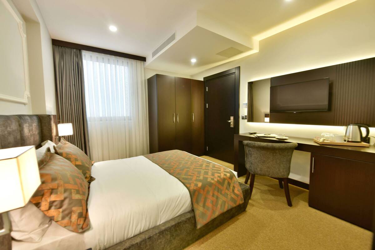 Een hotelkamer met een bed, een bureau, een stoel, een televisie en een raam met gordijnen.