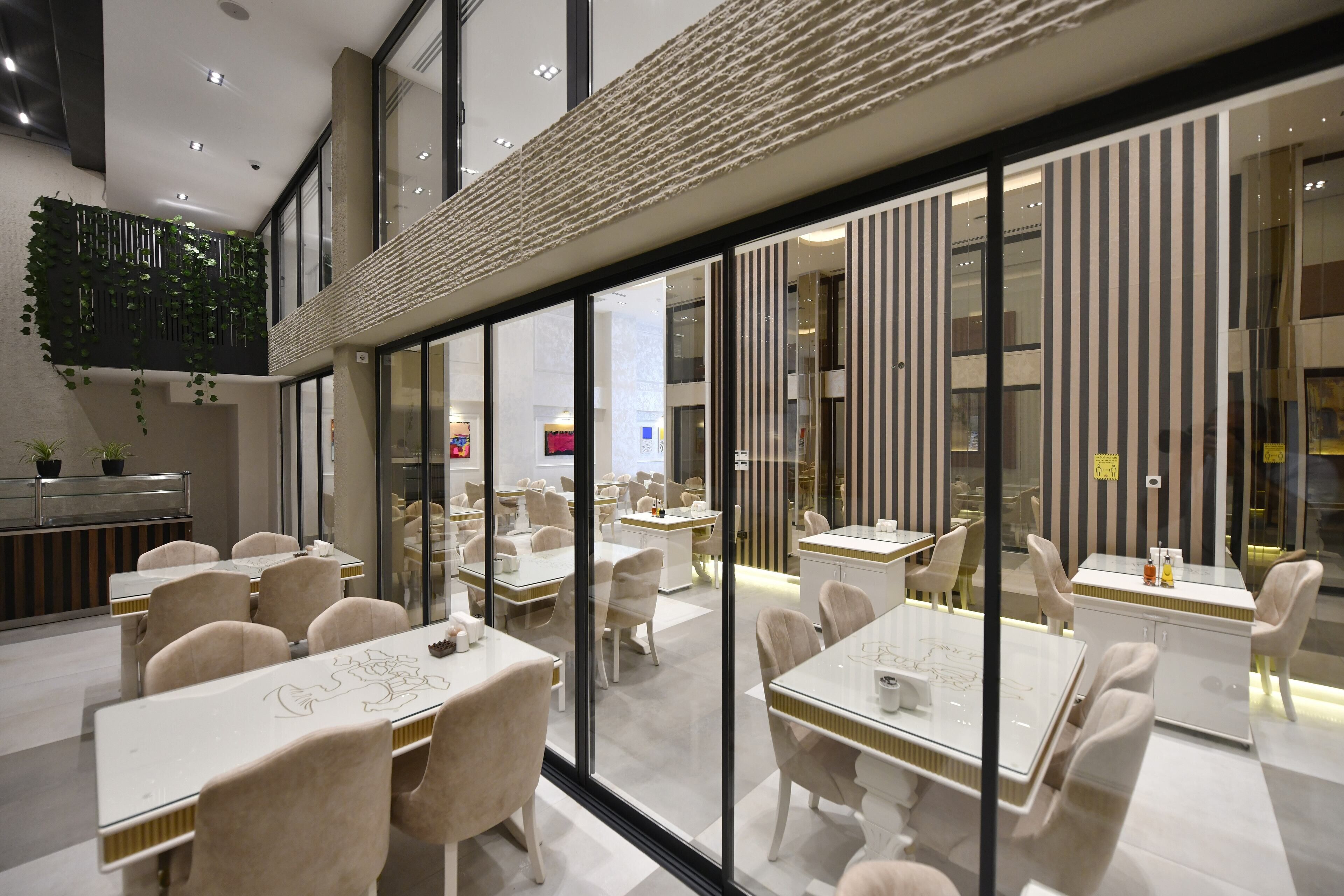 Un comedor moderno con separadores de vidrio, mesas blancas y sillas color beige.