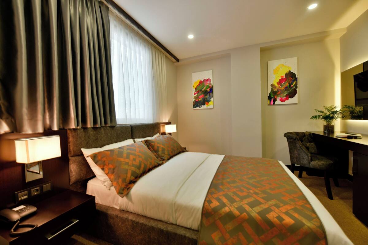 Een hotelkamer met een bed, een bureau, een stoel, een telefoon en twee schilderijen aan de muur.