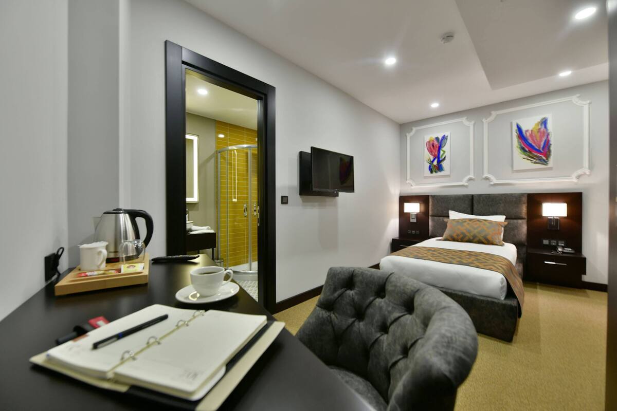 Hotelkamer met een bed, bureau met stoel, koffiezetapparaat, televisie en kunstwerken aan de wanden.
