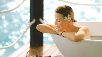 A woman relaxing in a bathtub with a wooden table and teapot in front of her.