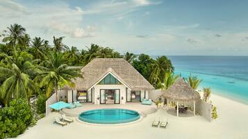 A beachfront property with a pool, lounge chairs, and a thatched-roof building.