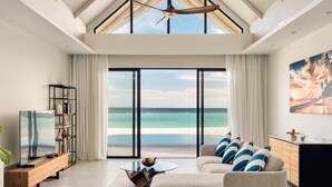 Un soggiorno moderno con un'ampia vetrata che si apre su una vista mare, un divano con cuscini blu e bianchi, un tavolino in legno e una libreria.