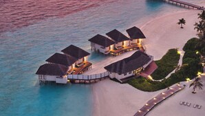 Bungalow sull'acqua con tetti in paglia collegati da passerelle, affacciati su una spiaggia con acque turchesi cristalline.
