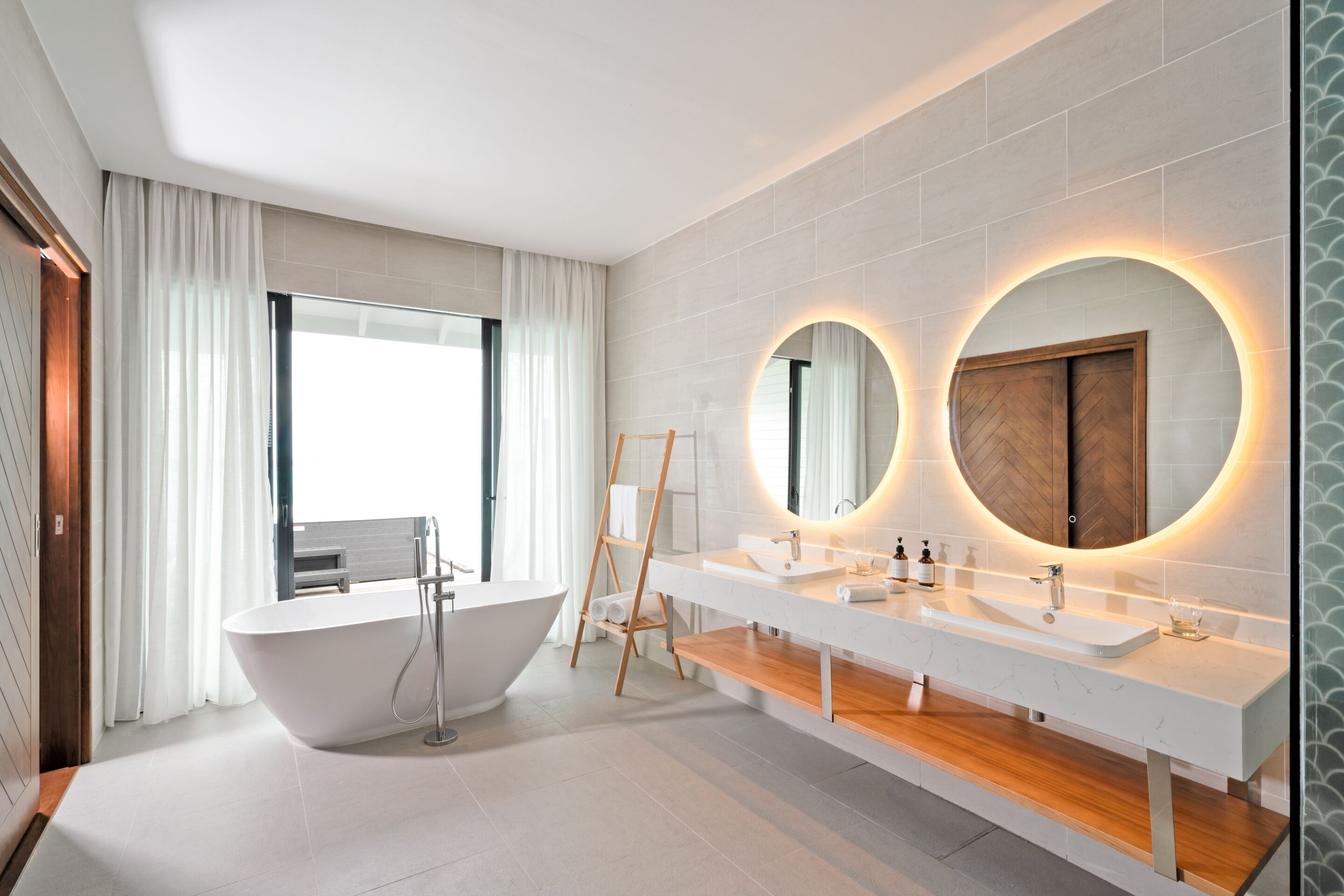 Un baño moderno con una bañera independiente, lavamanos dobles y un espejo grande con iluminación circular.