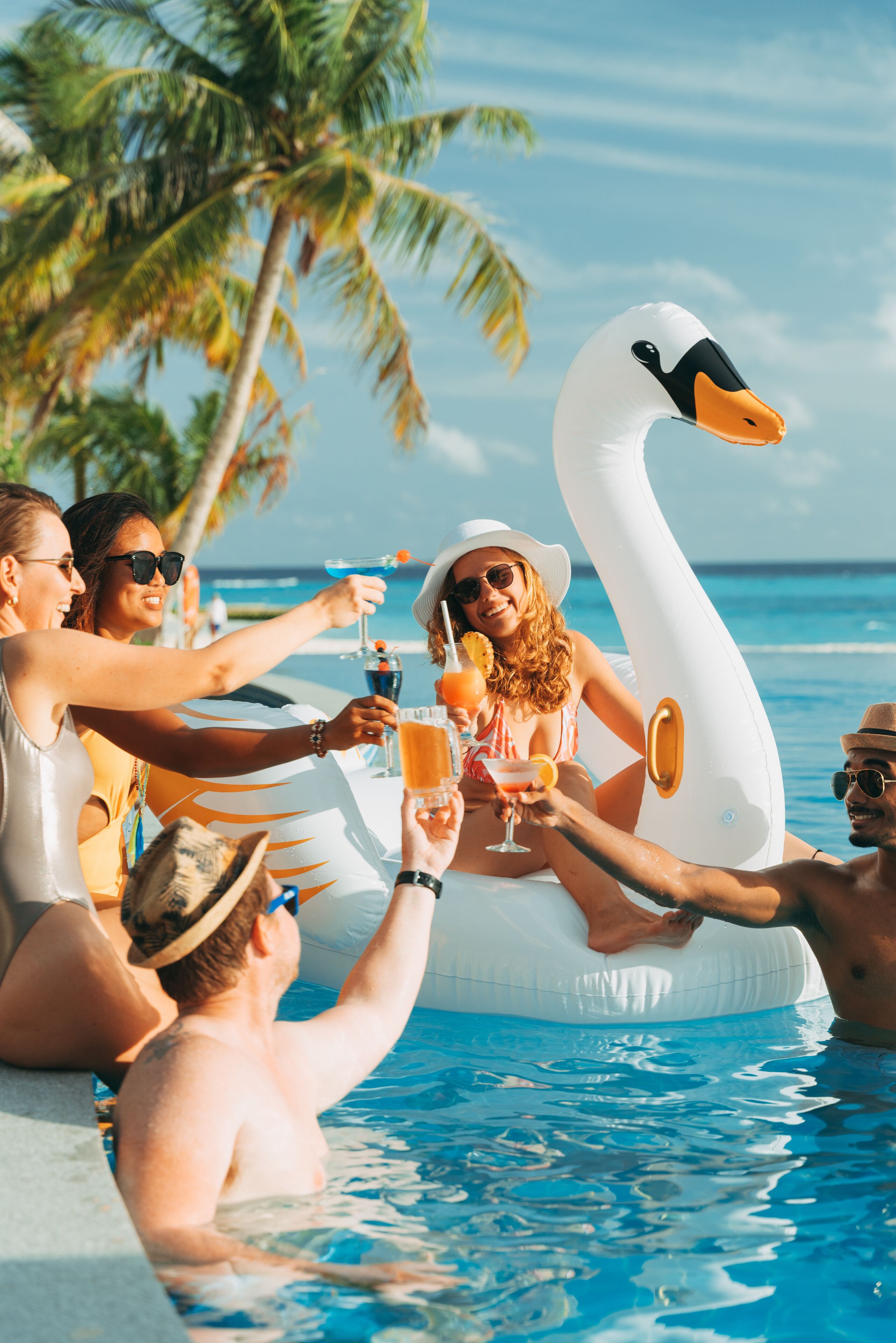 Un gruppo di persone brinda con bevande in una piscina con un galleggiante a forma di cigno.