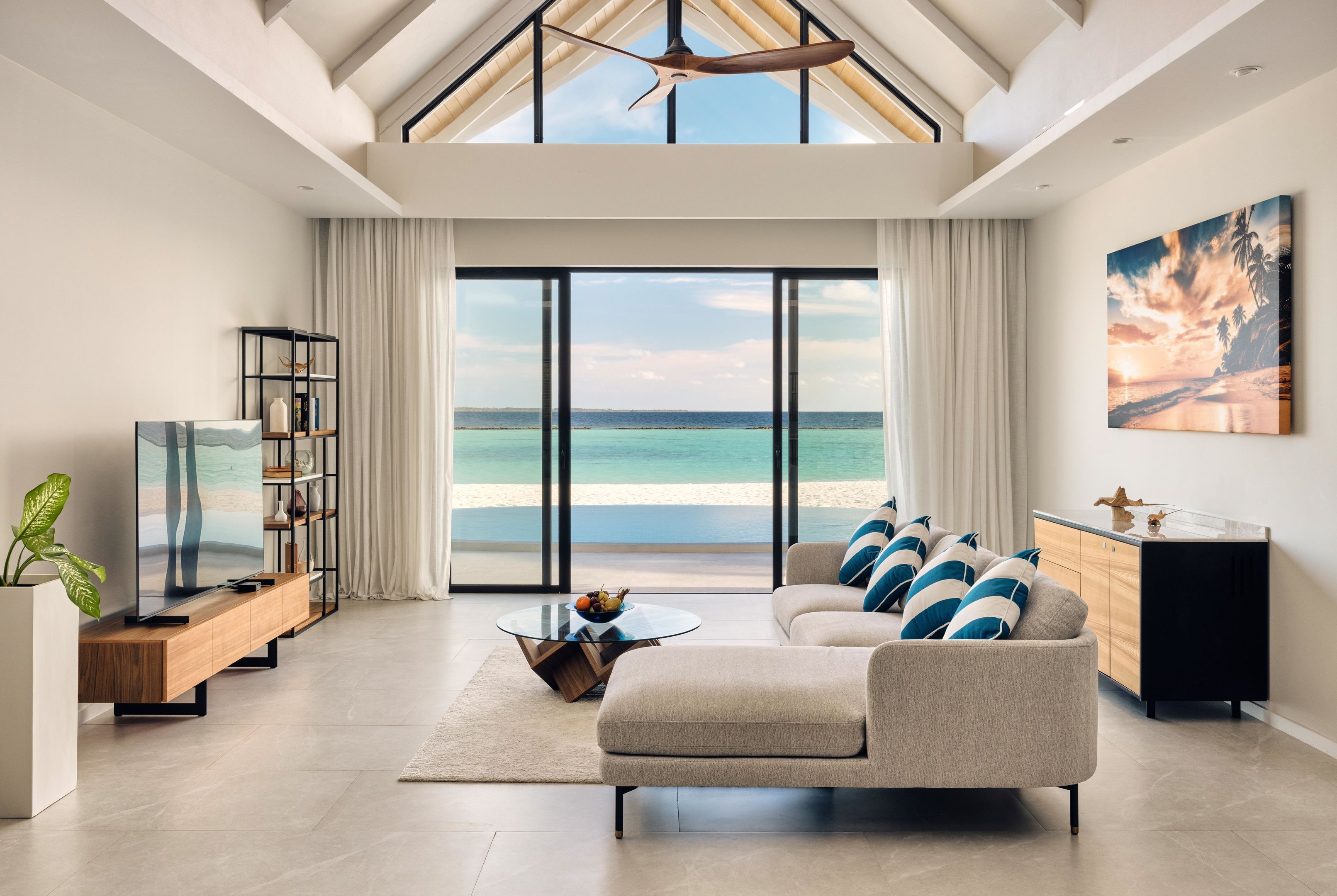 A spacious living room with a large window overlooking a beach, a ceiling fan, and a modern sofa.