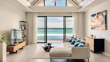 A spacious living room with a large window overlooking a beach, a ceiling fan, and a modern sofa.