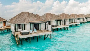 Bungalow sull'acqua con terrazze in legno e porte in vetro, collegate da passerelle, in un mare color turchese.