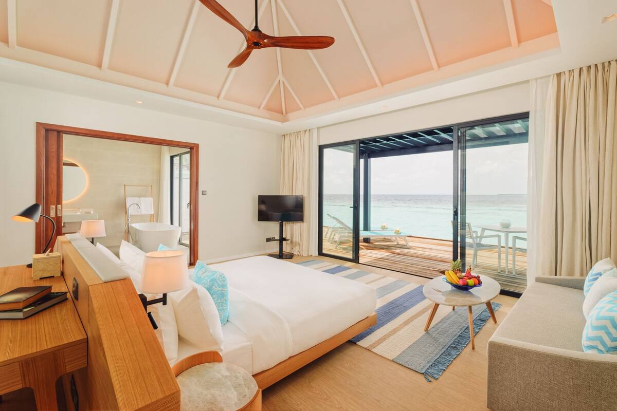 Et moderne hotelværelse med en stor seng, et skrivebord, et fjernsyn og en balkon med udsigt over havet.
