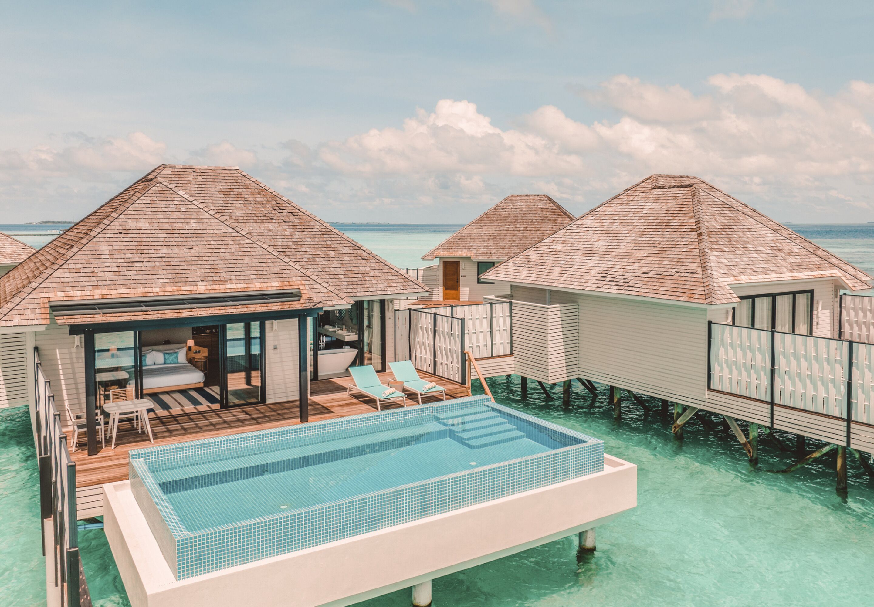 Overwater bungalows with a swimming pool, deck chairs, and a view of the ocean.