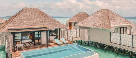 Overwater bungalows with a swimming pool, deck chairs, and a view of the ocean.