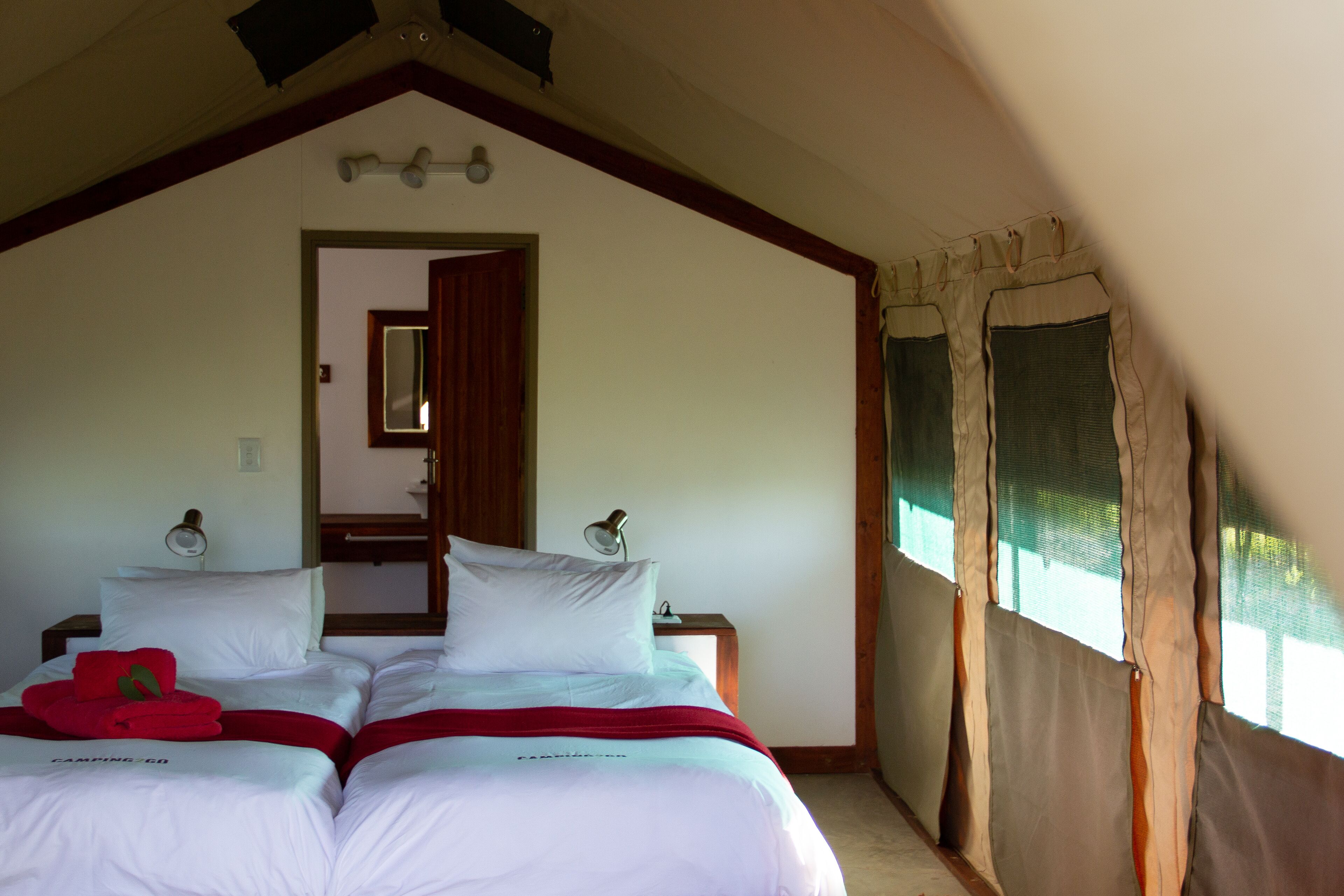 Un dormitorio con dos camas, techo de madera, una puerta que da a otra habitación y una ventana con cortinas.