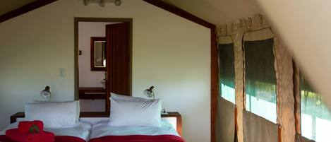 Un dormitorio con dos camas, techo de madera, una puerta que da a otra habitación y una ventana con cortinas.