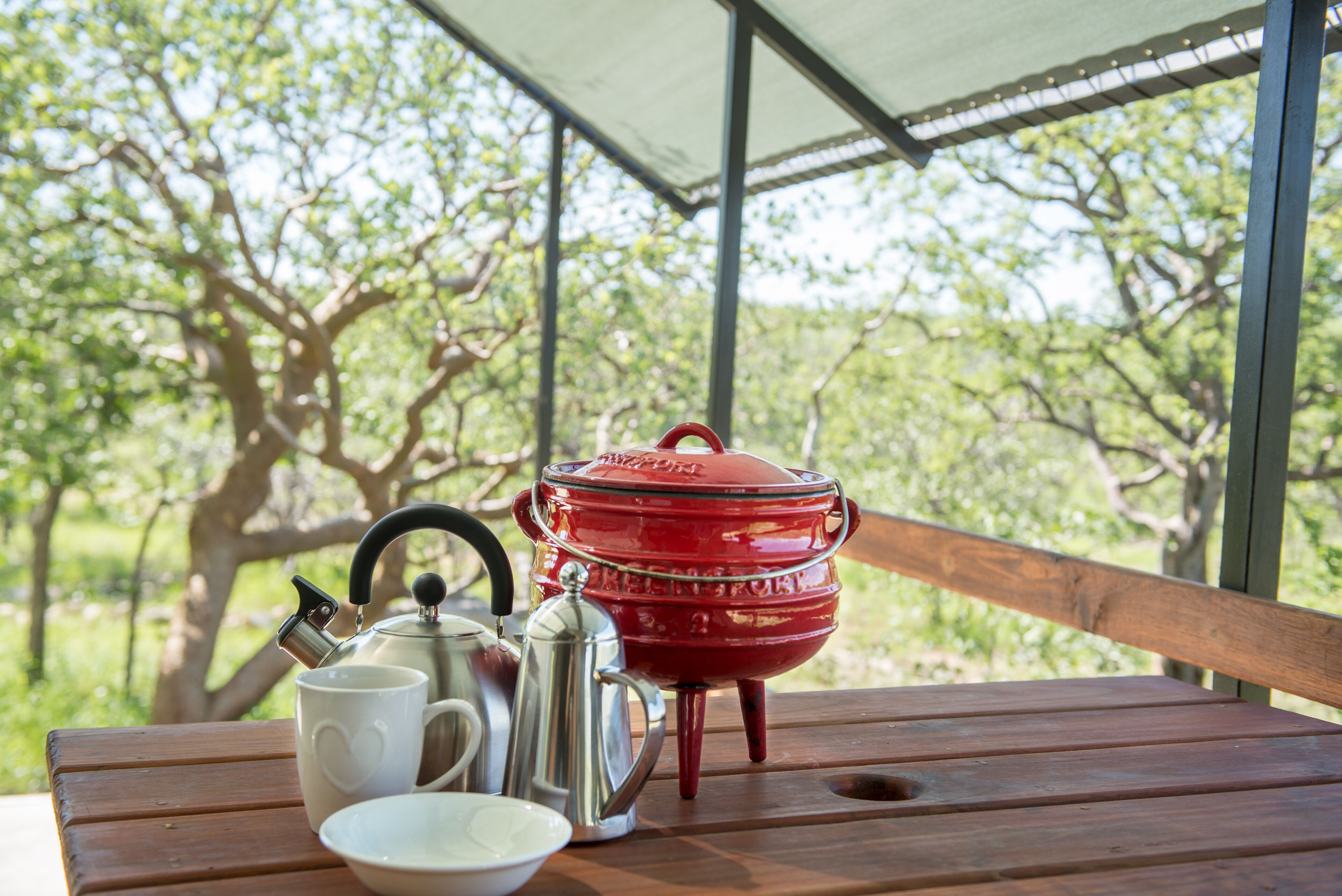 A wooden table with a red pot, a white mug, and a silver teapot.