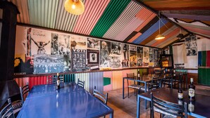 Un restaurante con un techo y paredes de metal corrugado de colores, decoradas con diversos carteles y fotografías. Mesas y sillas dispuestas para comer.