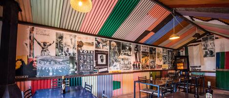 A restaurant with a colorful corrugated metal ceiling and walls adorned with various posters and photographs. Tables and chairs are arranged for dining.