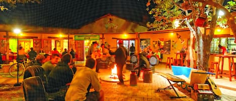 Un área de comedor al aire libre con suelo de ladrillo, mesas y sillas, y un pozo de fuego en el centro.